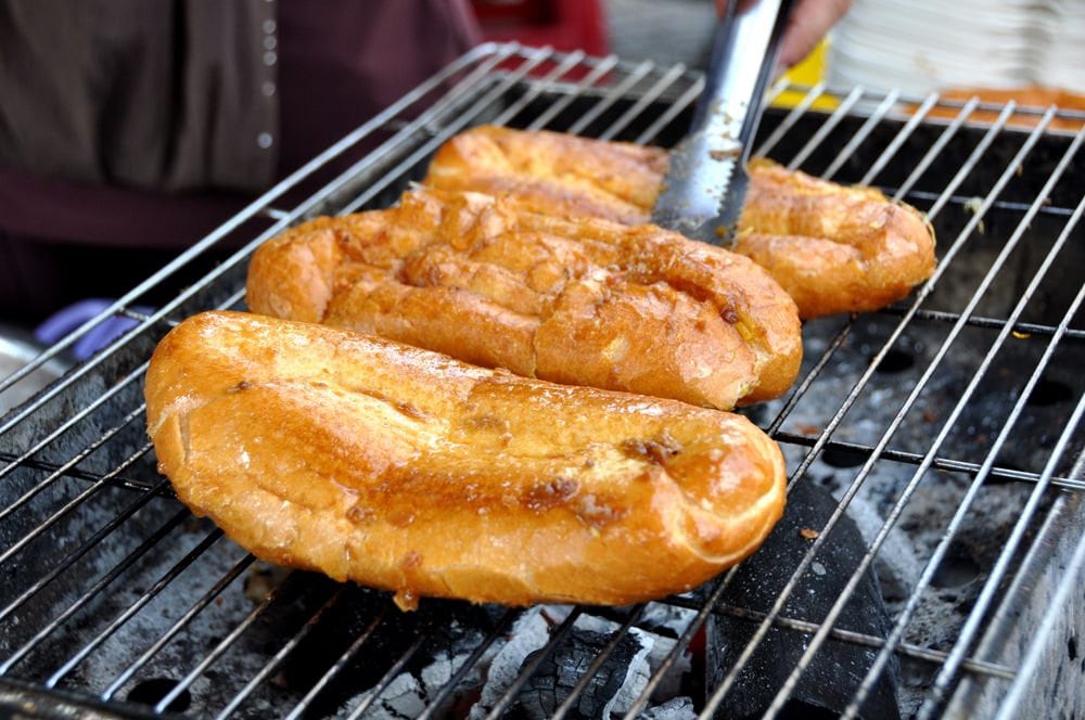 The banh mi is evenly coated with a layer of salt and chili sauce, then grilled to a golden crisp over charcoal